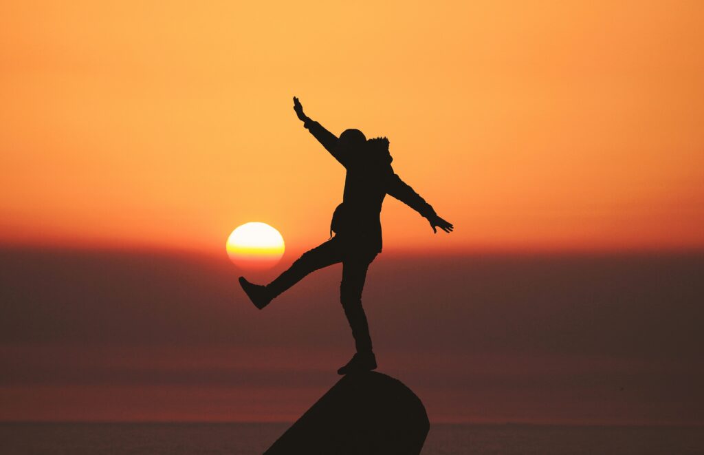 a man balancing on a rock at sunset pretending to kick the descending sun