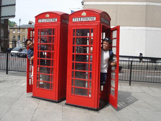 two red london phoneboxes with two people waving out of their open doors
